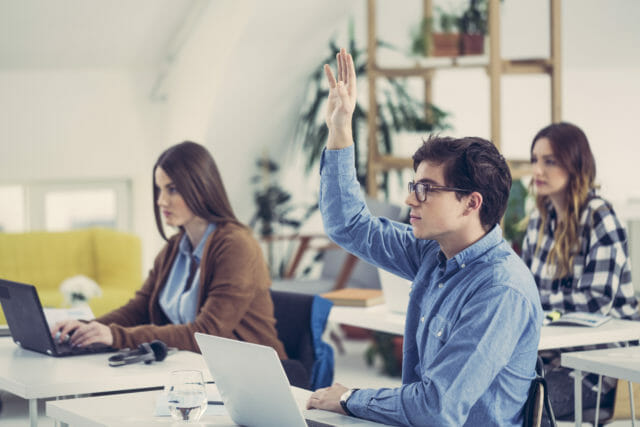 Man raising his hand in a classroom. Woman sitting next to him