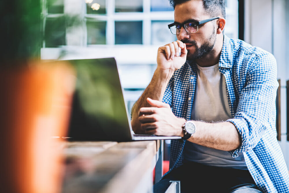 Man sitting in a cafe looking at his laptop while thinking