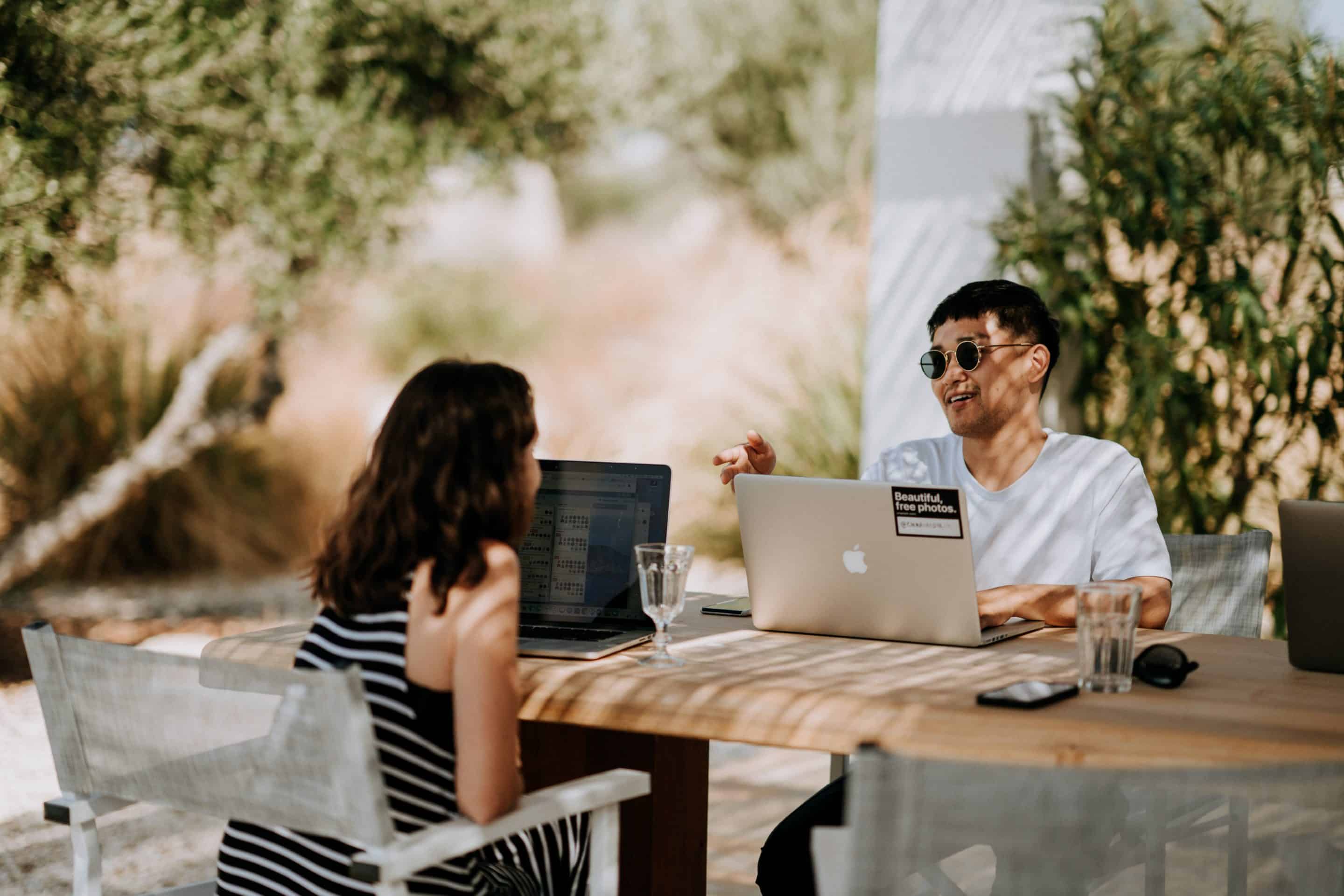 Two people sitting outside at a table with their laptops.
